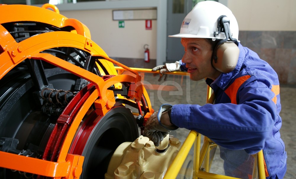 Operaio, con casco, occhiali protettivi e cuffie antirumore, in sala macchine controlla il funzionamento dell'eccitatrice di una turbina