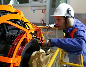 Operaio, con casco, occhiali protettivi e cuffie antirumore, in sala macchine controlla il funzionamento dell'eccitatrice di una turbina