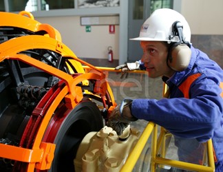 Operaio, con casco, occhiali protettivi e cuffie antirumore, in sala macchine controlla il funzionamento dell'eccitatrice di una turbina
