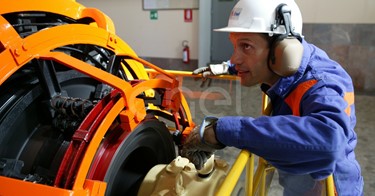 Operaio, con casco, occhiali protettivi e cuffie antirumore, in sala macchine controlla il funzionamento dell'eccitatrice di una turbina