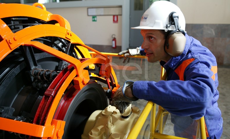 Operaio, con casco, occhiali protettivi e cuffie antirumore, in sala macchine controlla il funzionamento dell'eccitatrice di una turbina
