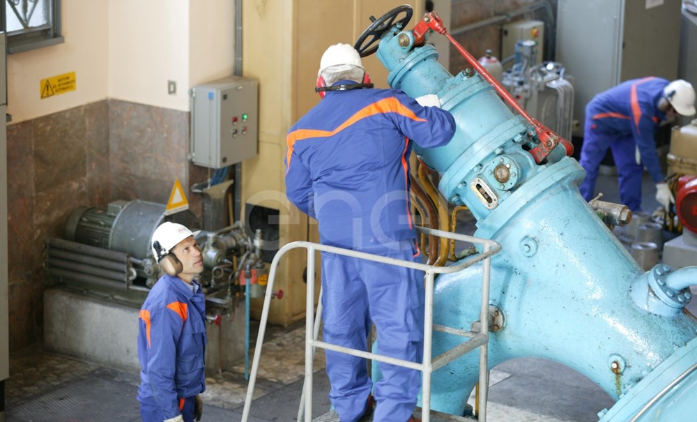 Operai, con casco, occhiali protettivi e cuffie antirumore, in sala macchine controllano il gruppo turboalternatore