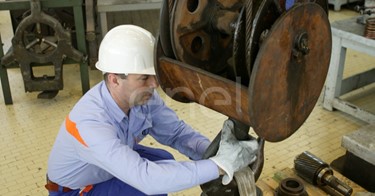 Operai agganciano una ruota dentata al carro ponte all'interno dell'officina della centrale di Sulcis