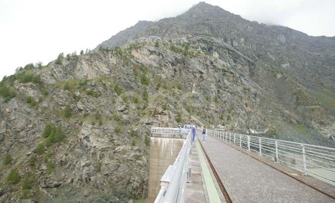 Coronamento della diga di Alpe Gera con operaio e turisti