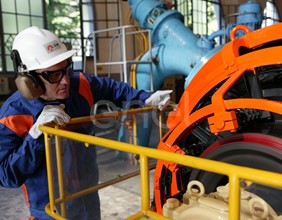 Operaio, con casco, occhiali protettivi e cuffie antirumore, in sala macchine controlla il funzionamento dell'eccitatrice di una turbina