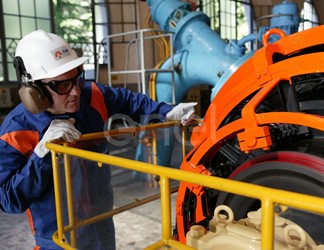 Operaio, con casco, occhiali protettivi e cuffie antirumore, in sala macchine controlla il funzionamento dell'eccitatrice di una turbina