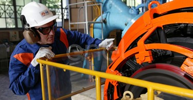 Operaio, con casco, occhiali protettivi e cuffie antirumore, in sala macchine controlla il funzionamento dell'eccitatrice di una turbina