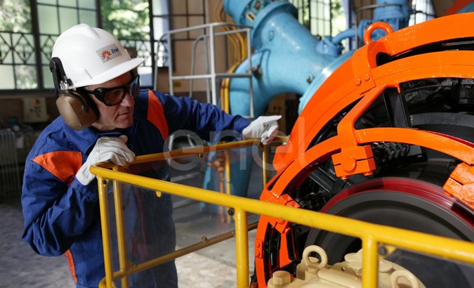 Operaio, con casco, occhiali protettivi e cuffie antirumore, in sala macchine controlla il funzionamento dell'eccitatrice di una turbina