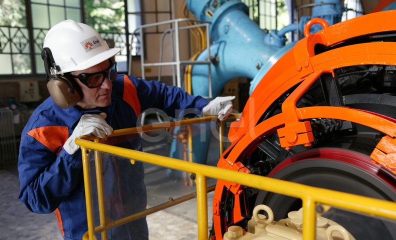 Operaio, con casco, occhiali protettivi e cuffie antirumore, in sala macchine controlla il funzionamento dell'eccitatrice di una turbina