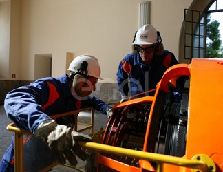 Due Operai, con casco, occhiali protettivi e cuffie antirumore, in sala macchine controllano il funzionamento dell'eccitatrice di una turbina