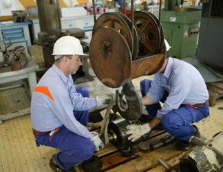 Operai agganciano una ruota dentata al carro ponte all'interno dell'officina della centrale di Sulcis