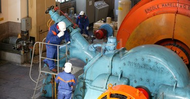 Operai, con casco, occhiali protettivi e cuffie antirumore, in sala macchine controllano il gruppo turboalternatore