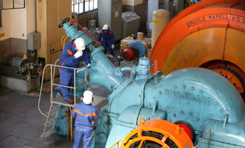 Operai, con casco, occhiali protettivi e cuffie antirumore, in sala macchine controllano il gruppo turboalternatore